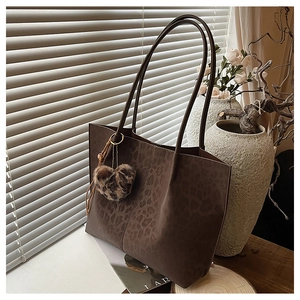 Detail of leopard print tote bag with plush heart charm in a warm aesthetic setting