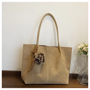 Detail of khaki suede tote bag featuring a leopard heart charm and leather tassel accents