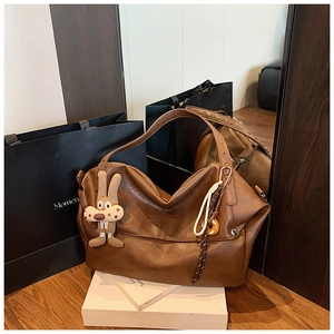 Close-up of vintage brown tote bag featuring plush rabbit and braided rope pendants
