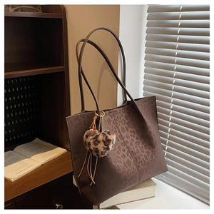 Macro detail of leopard print tote bag with plush heart charm on a wooden shelf