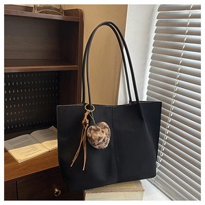 Detail of black leather tote bag with leopard fur ball and tassels by a vintage bookshelf