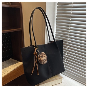 Detail of large black tote bag featuring leopard print pom-pom and leather tassel charm