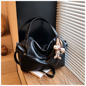 Detail of slouchy black faux leather tote with woven strap and plush monkey charm