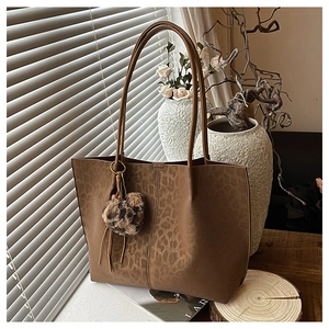Brown leopard print tote bag with plush heart charm and tassel in a cozy setting