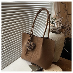 Detail of a brown tote bag with subtle leopard print and a plush heart tassel charm