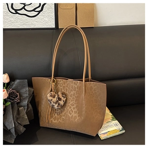 Detail of leopard print tote bag with plush heart charm on a black leather sofa