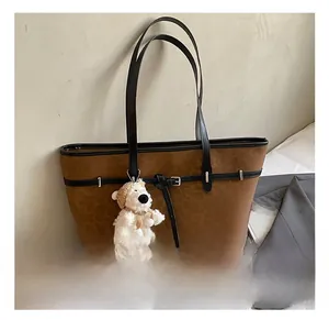 Detail of leopard print tote bag featuring black leather handles and a plush bear charm