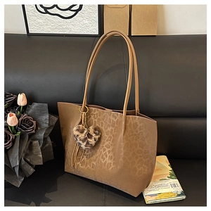 Detail of leopard print tote bag with plush heart charm on a black leather sofa
