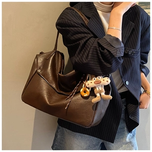 Detail of dark brown faux leather shoulder bag with side buckle and plush doll pendant