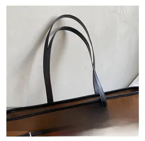 Detail view of the brown leather tote bag handle and metal buckle with litchi grain texture