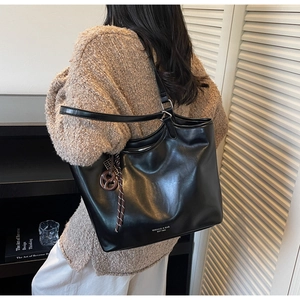 Detailaufnahme einer schwarzen Leder-Tote-Bag mit Markenschriftzug und braunem Anhänger