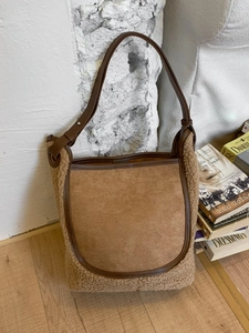 Secchiello in camoscio marrone e shearling con tracolla in pelle in un ambiente minimalista