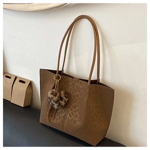 Detail of leopard print tote bag featuring a plush heart charm and long handles