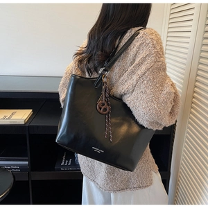 Detailansicht der schwarzen Leder-Tote-Bag mit Brezel-Anhänger und weißem Logo-Aufdruck