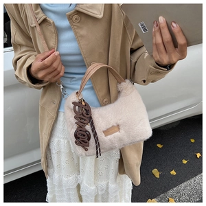 Detailansicht der beigefarbenen Kunstfell-Handtasche mit braunen Ledergriffen und Anhänger
