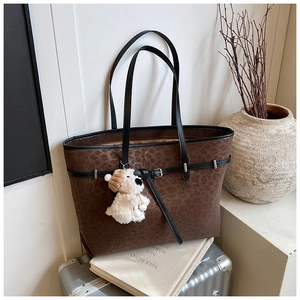 Detail of leopard print tote bag with black leather handles and plush puppy charm decor