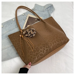 Close-up of leopard print tote bag with plush pom-pom and leather tassel details