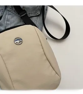 Detail of a beige oxford fabric crossbody bag featuring a round metal logo plaque