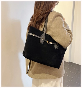 Detail of large black suede tote bag with slim shoulder strap and gold buckle accent