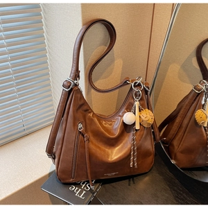 Detail of dark brown faux leather hobo bag with baseball charm and stylish fringe zip