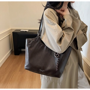 Detail der dunkelbraunen Leder-Shopper mit schmalen Riemen und rundem Anhänger-Dekor