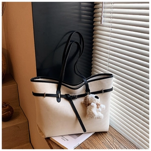 Detail of off-white tote bag featuring black leather trim and cute plush puppy charm