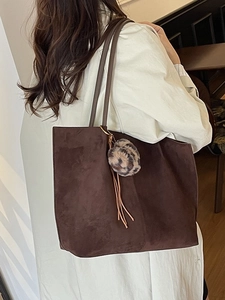 Large dark brown suede tote bag with leopard fur ball and tassels shown on a model