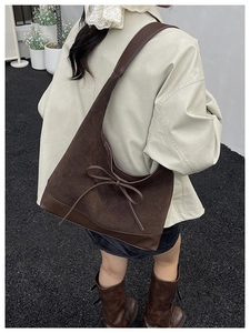 Outdoor shot of large dark brown suede tote bag with leather bow detailing and strap