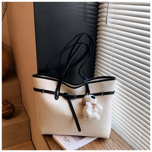 Close-up of beige faux leather tote bag featuring black trim and a cute plush bear charm