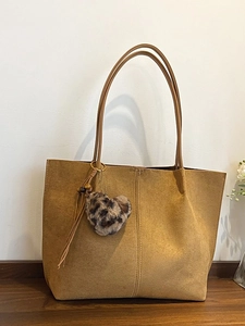Brown faux suede tote bag with leopard heart charm and tassel detail on wooden surface