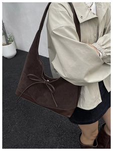 Outdoor model shot of a dark brown suede tote bag featuring a leather bow tie detail