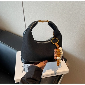 Détail d'un sac à main en toile noire avec boucle dorée et breloque en perles de bois