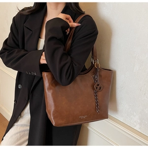 Detail der dunkelbraunen matten Shopper-Tasche mit Goldlogo und gewebtem Anhänger