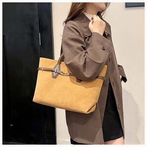 Close-up of matte suede tote bag with brown leather handles and gold metal buckle detail