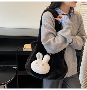 Large black plush tote bag with white bunny detail shown on a model in a modern interior