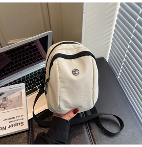 Close-up of beige nylon crossbody bag with circular metal logo and black zip closure