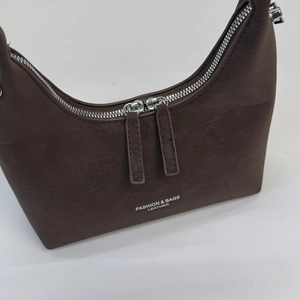 Detail of a brown leather crescent bag showing top metal zippers and embossed logo texture
