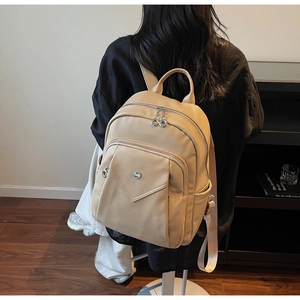 Close-up of beige faux leather backpack with silver zippers and multi-pocket design