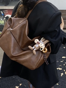 Retro brown large capacity shoulder bag with plush pendant on a model in autumn street