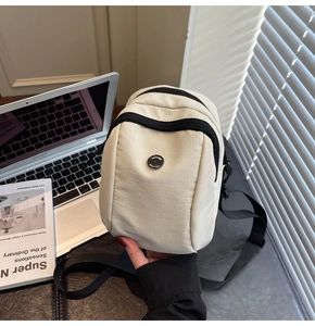 Detail of off-white canvas crossbody bag with dual zippers and circular metal logo