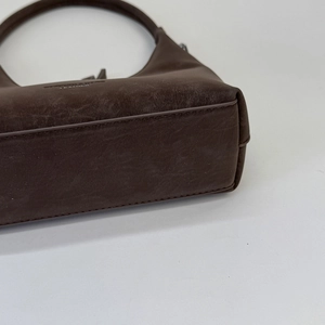 Detail of dark brown vintage leather dumpling bag with reinforced stitching and embossed text