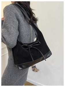 Detail of black suede hobo bag featuring slim bow accent and smooth leather patchwork
