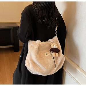 Detail van pluche crossbodytas met beerhanger en leren logo in een warm interieur