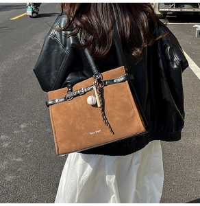 Brown suede tote bag with black leather trim and baseball pendant shown on shoulder