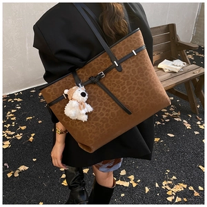 Detail of leopard print tote bag with plush bear charm and leather strap on ginkgo leaves