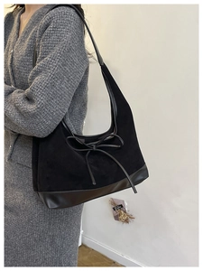 Detail of black suede tote bag with minimalist leather bow accent and polished base