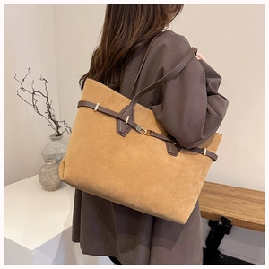 Detail of caramel suede tote bag with leather straps and golden metal buckle on a pedestal