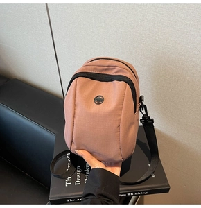 Mini pink nylon crossbody bag detail with black zipper pocket and round metal badge