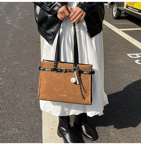 Detail of brown suede tote bag with black leather straps and baseball charm