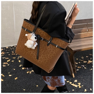Detail of leopard print tote bag with plush puppy pendant carried by a model outdoors